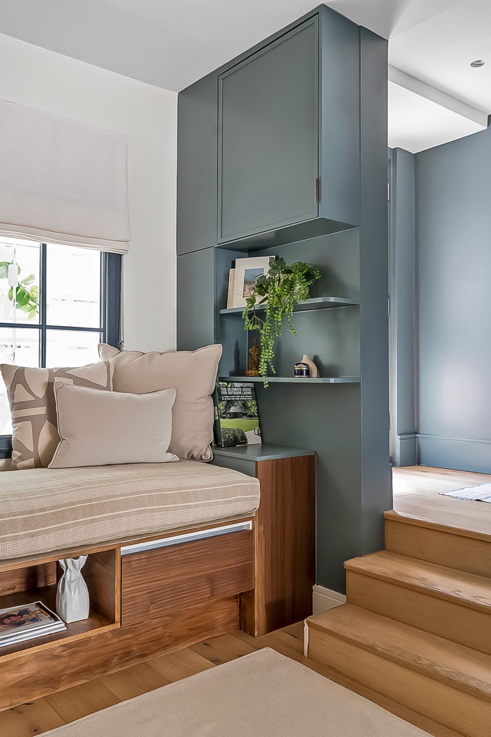 Blue-grey fitted cabinetry and open shelving beside a raised window seat