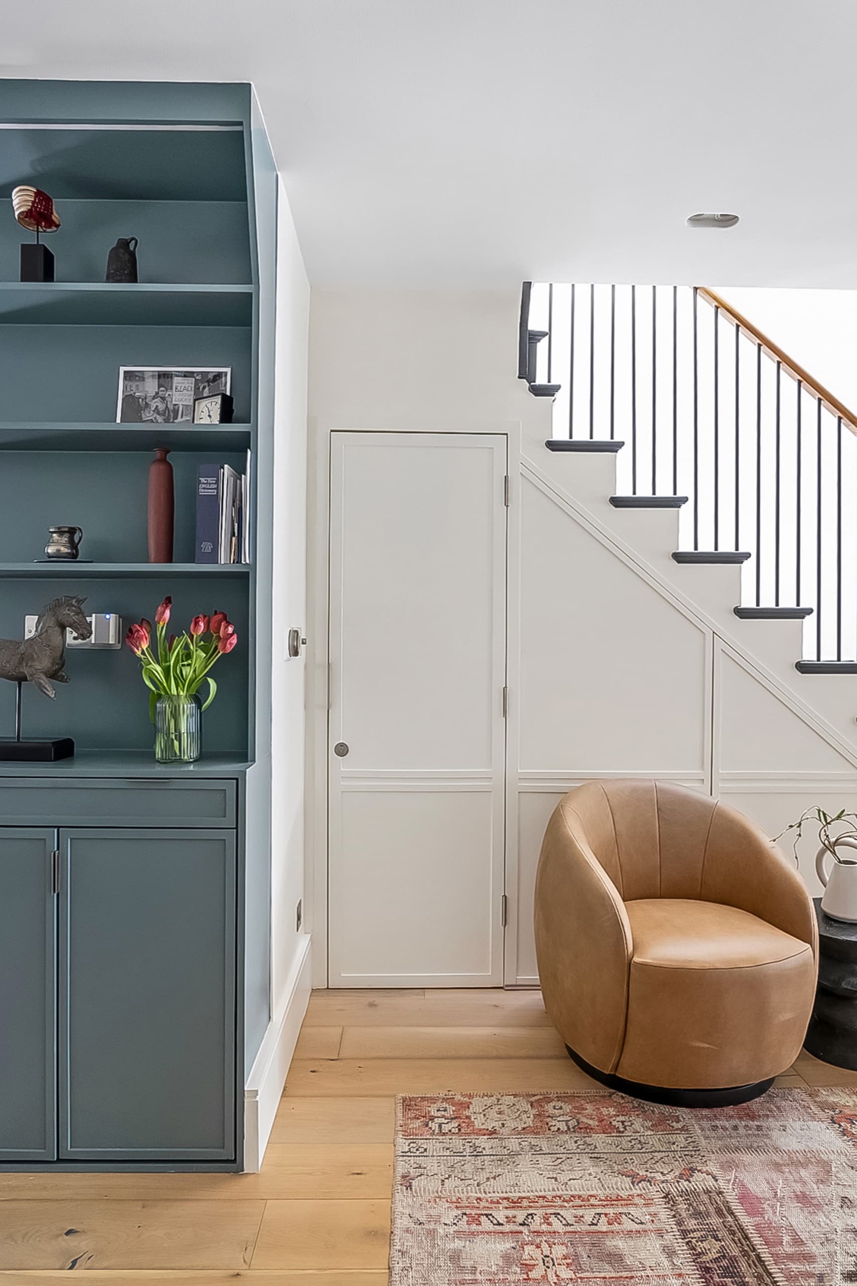 Hallway with a blue-grey bookcase, tan leather swivel chair and fitted understairs storage