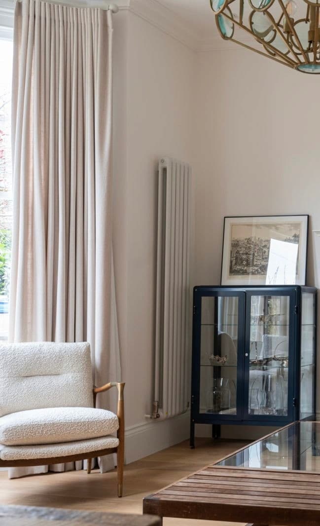 Living room corner with a bouclé armchair, column radiator and a glazed navy display cabinet