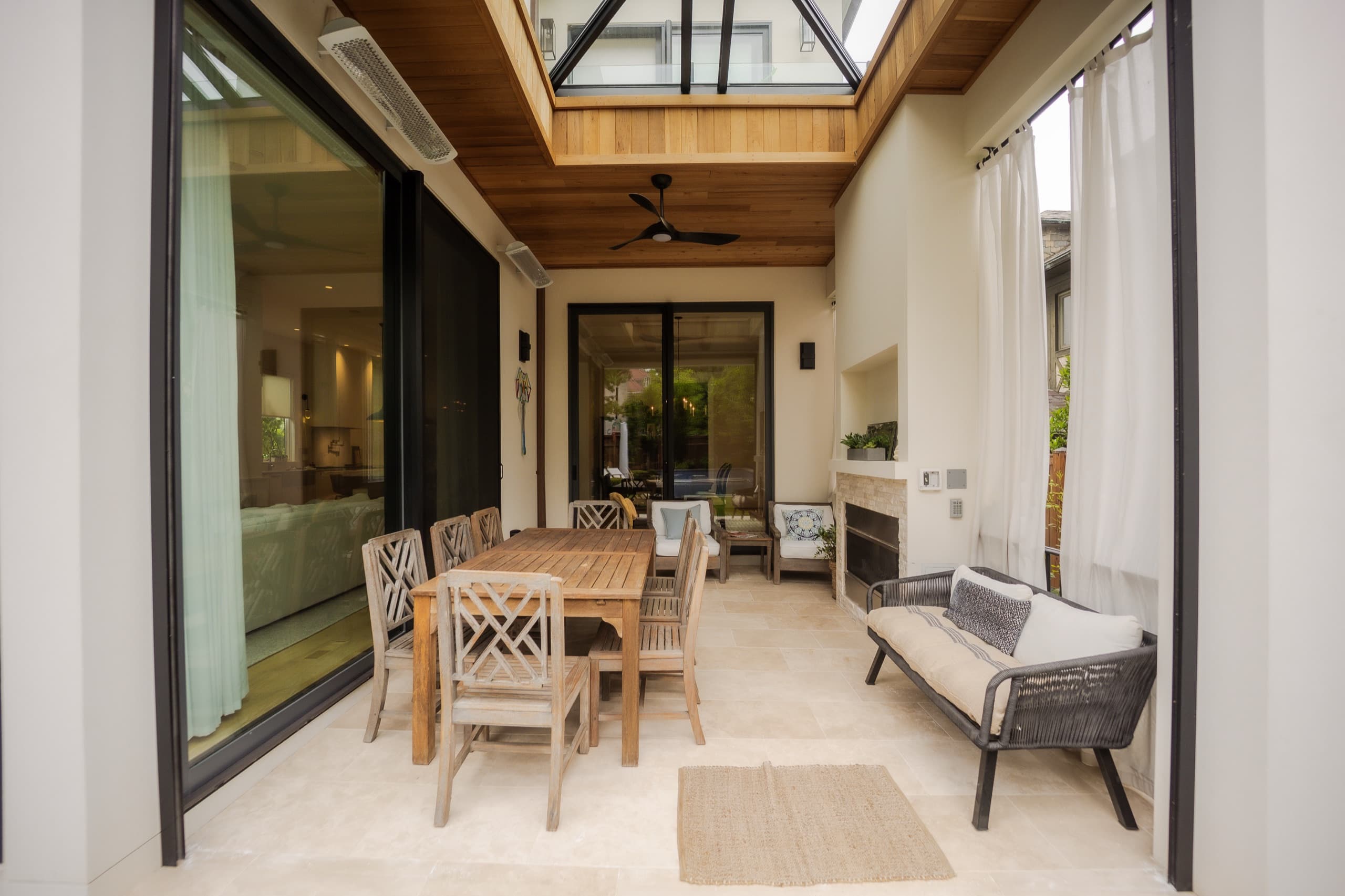 Covered outdoor dining loggia with a glazed roof lantern, timber ceiling and an outdoor fireplace