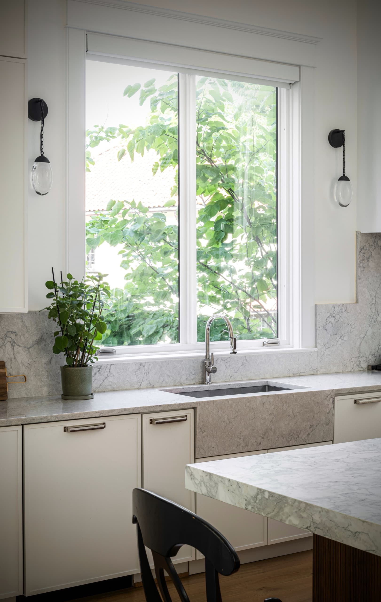 Marble-topped kitchen counter beneath a garden window, flanked by glass wall sconces
