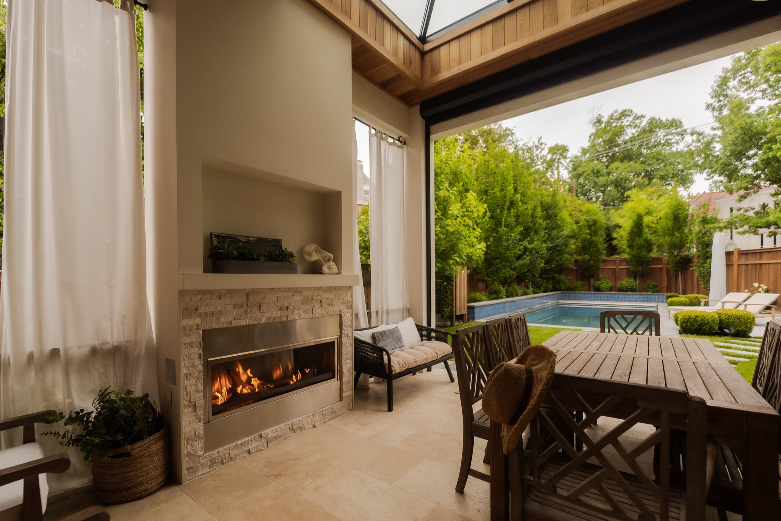 Outdoor loggia with a lit gas fire, looking out across the pool and garden