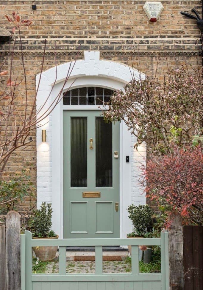 Sage-green panelled front door with an arched fanlight, set in London stock brick