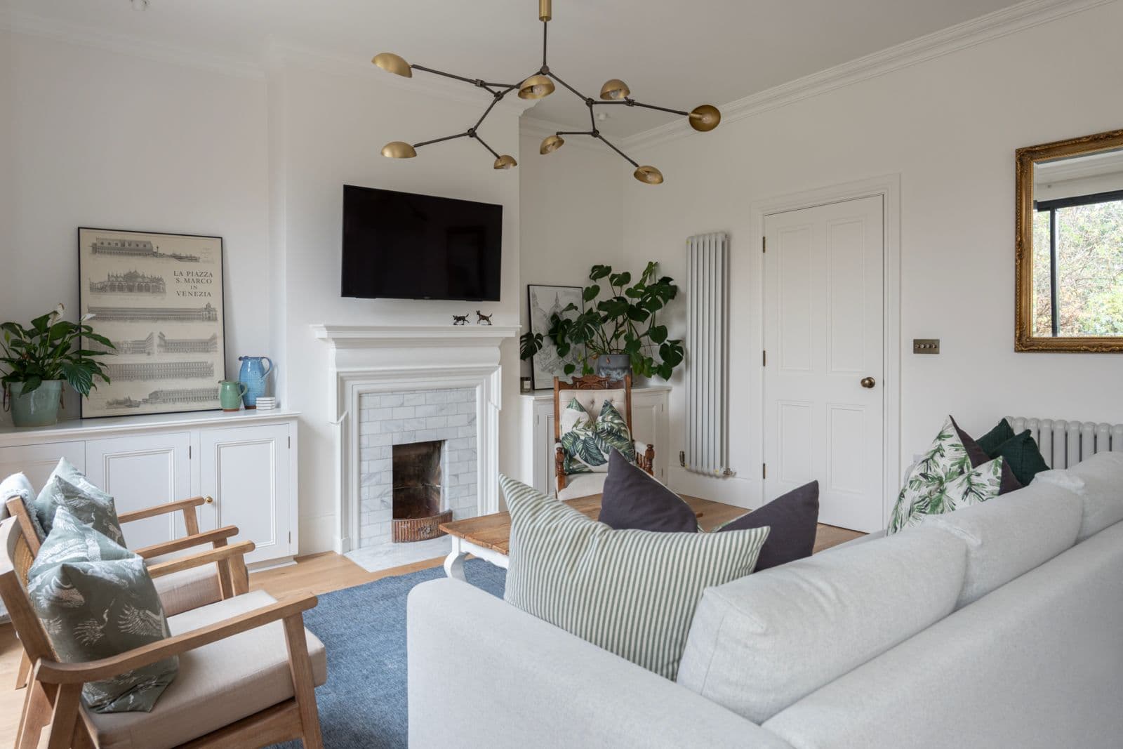 Family living room with a marble fireplace, brass branched pendant and a blue wool rug